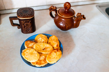 Rustic vintage antique traditional teapot and mug from Carpathian region of Ukraine with plate of fried cottage cheese pancakes on table