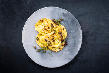 Traditional Italian ravioli pasta offered with capers and onion chili pesto as top view on a modern design plate with copy space