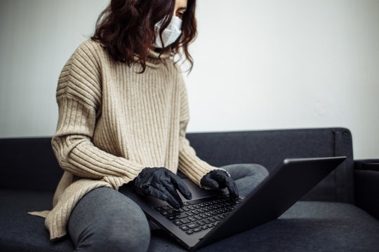 Young woman working from home during quarantine due to coronavirus pandemia. Beautiful girl stays home wearing medical mask and gloves and typing on a laptop. Covid-19 epidemia worldwide concept. - Powered by Adobe