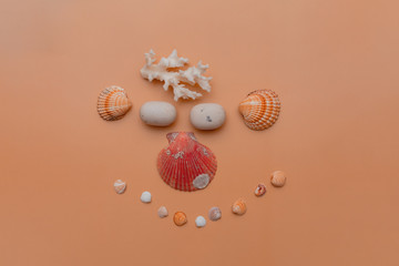 Seashells of various kinds, white stones and coral, laid out in the form of faces, on a beige background. Flat lay, copy space, feed from above, creative. The concept of vacation, tourism, summer.