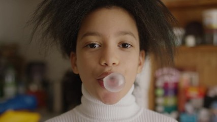 Beautiful young girl blowing bubble gum towards camera and laughing after, in slow motion