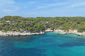 Fototapeta na wymiar Tranquil summer landscape in Menorca, Spain. Turquoise sea, cliffs with pine trees, blue sky and light clouds.