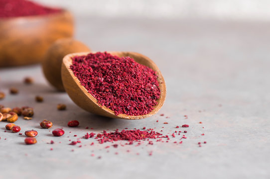 Dried ground red Sumac powder spices in wooden spoon with sumac berries on rustic table. Healthy food concept