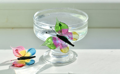 Obraz na płótnie Canvas colored glass butterflies on a cup of water on a white background