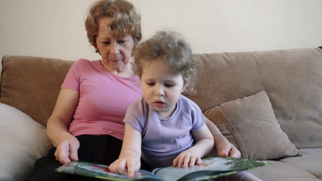 Grandmother and granddaughter together reading a book and view pictures. Happy grandmother nanny teaching grandkid learning reading at home. Grandparent and grandchild activity concept.