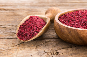 Obraz na płótnie Canvas Dried ground red Sumac powder spices in wooden spoon and bowl on rustic table. Healthy food concept