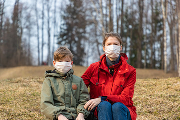 Young woman with boy wearing medical face masks to protect themselves from coronavirus on the abandoned park during quarantine. Corona virus, covid -19, pandemic protection concept.
