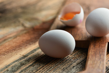 Chicken eggs and half broken egg with yolk on wooden background.