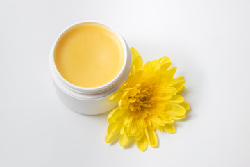 Obraz na płótnie Canvas Container of yellow cosmetic cream and flower on white background. Handmade organic cosmetics, facial care. Professional cosmetic products