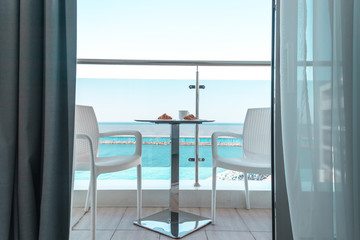Two white chairs with a table on which stands a breakfast of coffee and croissants on the balcony with sea view