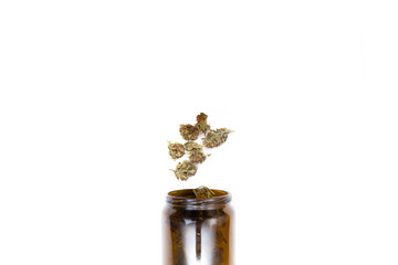 Obraz na płótnie Canvas Brown glass jar full of perfect green dried cannabis buds and several marijuana buds falling in it isolated on white background.