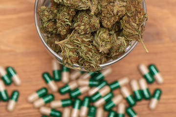Top down shot of glass full of green dried cannabis buds and some medical pills on wooden table. Marijauna buds and medical pills. Medical marijauna.