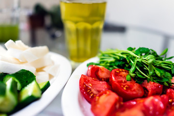 Ingredient cooking preparation or snack with closeup of plate with chopped sliced Japanese cucumbers, pea shoots, tomatoes and daikon radish with background of green tea