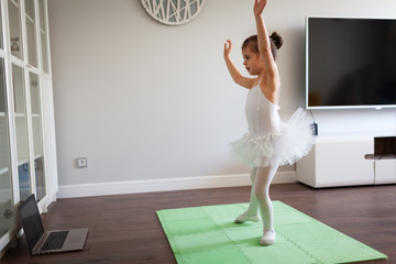 Pretty young ballerina practicing classic choreography during online class in ballet school, social...