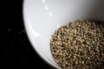 Close-up of Organic White quinoa seeds, in a small white porcelain bowl on a black background