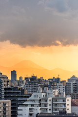 Yellow orange sunset in Tokyo, Japan Shinjuku cityscape with silhouette view of Mount Fuji and golden sunlight, apartment buildings and mountains during rain