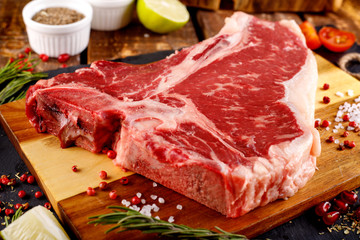 Raw T-bone Steak for grill or BBQ on cutting board over aged wooden background