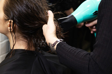 Fototapeta premium The hairdresser dries the girl’s wet long hair with a hairdryer in a beauty salon. The work of makeup artist. Middle angle