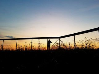 Person bebachtet Sonnenuntergang durch den Maschendrahtzaun
