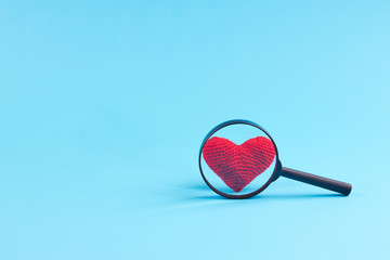 magnifier and heart symbol over it. blue background. heart disease concept. look to heart work.