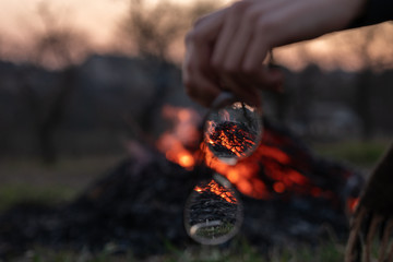 Camp fire through the glass of eyeglasses, blurred female hands holding glasses