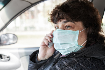 close up portrait of a woman with medical mask. Female person sitting in car and talking by mobile phone.