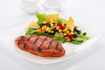 Mexican style marinated grilled chicken breast with fresh salads and green herb pesto on white rectangle plate