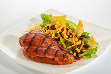 Mexican style marinated grilled chicken breast with fresh salads and green herb pesto on white rectangle plate