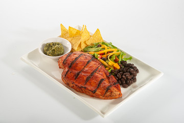 Mexican style marinated grilled chicken breast with fresh salads and green herb pesto on white rectangle plate
