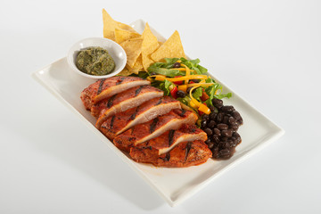 Mexican style marinated grilled chicken breast with fresh salads and green herb pesto on white rectangle plate