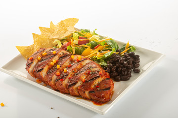 Mexican style marinated grilled chicken breast with fresh salads and green herb pesto on white rectangle plate