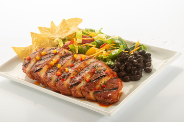 Mexican style marinated grilled chicken breast with fresh salads and green herb pesto on white rectangle plate