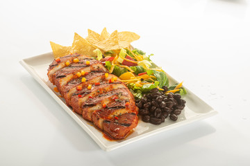 Mexican style marinated grilled chicken breast with fresh salads and green herb pesto on white rectangle plate