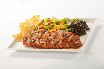 Mexican style marinated grilled chicken breast with fresh salads and green herb pesto on white rectangle plate