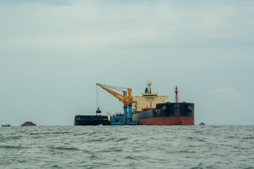 Loading coal from cargo barges onto a bulk vessel using ship cranes  in offshore coal cargo terminal.