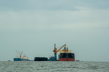 Loading coal from cargo barges onto a bulk vessel using ship cranes  in offshore coal cargo terminal.