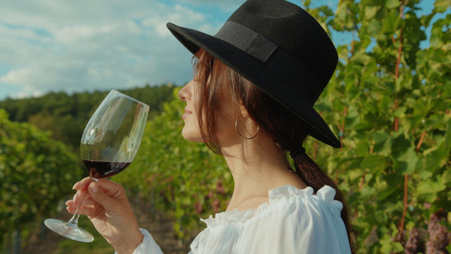 Inspired beautiful young lady enjoying wine taste holding glass walking with excitement in grape garden valley. Vineyard and people.
