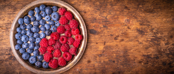 Ripe blueberries and raspberries in a bowl in the form of a yin and yang symbol on a wooden table - pan-frame background with copy space