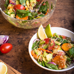 American vegetarian salad with vegetables, avacado, lettuce and quinoa in a plate with lime slices on a wooden table