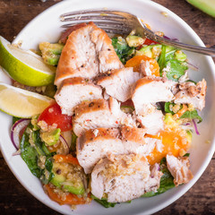 American delicious salad with chicken breast, vegetables, avacado, lettuce and quinoa in a plate close-up, top view