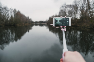 Mock Up white smartphone in the hands of a man on a background of nature, water and trees. concept on the theme of travel.