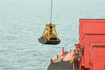 Fototapeta na wymiar Loading coal from cargo barges onto a bulk vessel using ship cranes in offshore coal cargo terminal. 