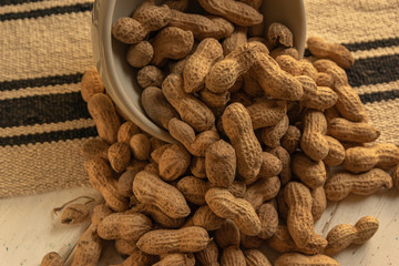 inshell peanuts in a white ceramic bowl on a cloth tablecloth and white wooden table