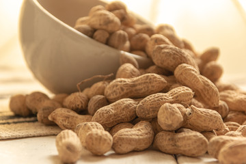 inshell peanuts in a white ceramic bowl on a cloth tablecloth and white wooden table