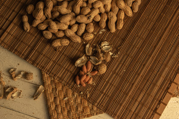 a scattering of peeled and unshelled peanuts on mats and a white wooden table
