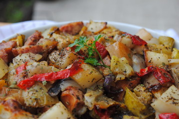 Roasted Vegetables and Sausages casserole sprinkled with seasonings, in a white ceramic bowl, close up view.