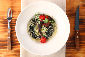 black pasta with octopus parmesan and cherry tomatoes on wooden background in white plate top view