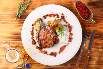 freshly grilled hot steaks with potato on wooden table and beer in glass top view