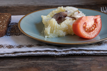 Cooking at home, in isolation, quarantine. Homemade rustic bread, herring, mashed potatoes, tomato in a plate on a wooden background in the home kitchen.