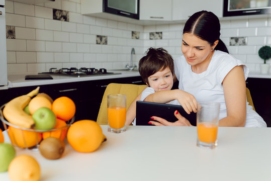 Family using a tablet pc in kitchen, mother with son happy smile, modern kitchen orange juice